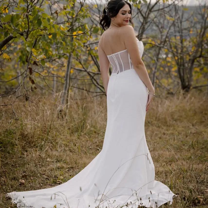 Back of the Dress Photo: Back view of the bride in the Allure wedding gown, showcasing the fit-and-flare draped skirt and long train, with the elegant details of the overlay bodice visible.