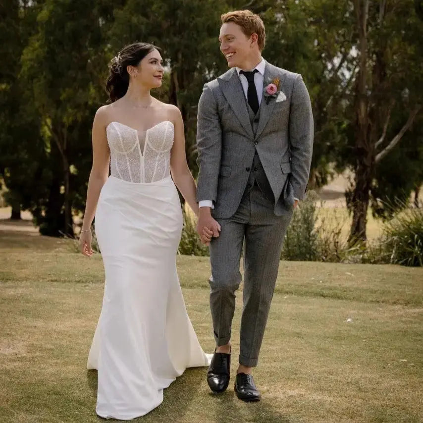 Bride in Kara Wedding Gown with beaded tulle overlay, corset bodice, and fit and flare skirt walking with groom outdoors