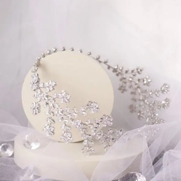 Elegant Lena Bridal Tiara with shimmering floral blossoms and silver crystal CZ embellished leaves, cascading delicately over the side of the headband, perfect for a glamorous bridal hairstyle.