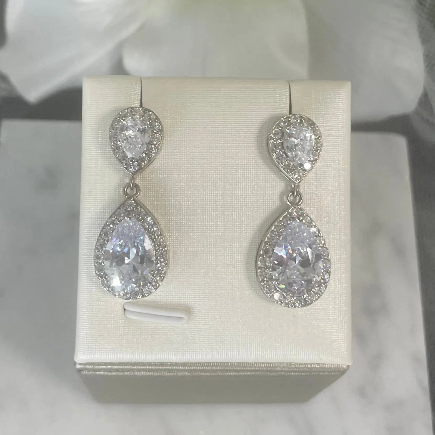 Leona Earrings (Silver): Elegant silver earrings with a large CZ stone surrounded by smaller CZs, offering a sophisticated drop design.