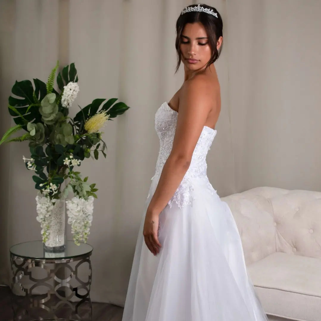 A debutante beams in the Libby A-line Tulle Deb Dress, featuring a flattering sweetheart neckline and bodice adorned with delicate lace appliqué, leading down to a full tulle skirt that softly brushes the ground.