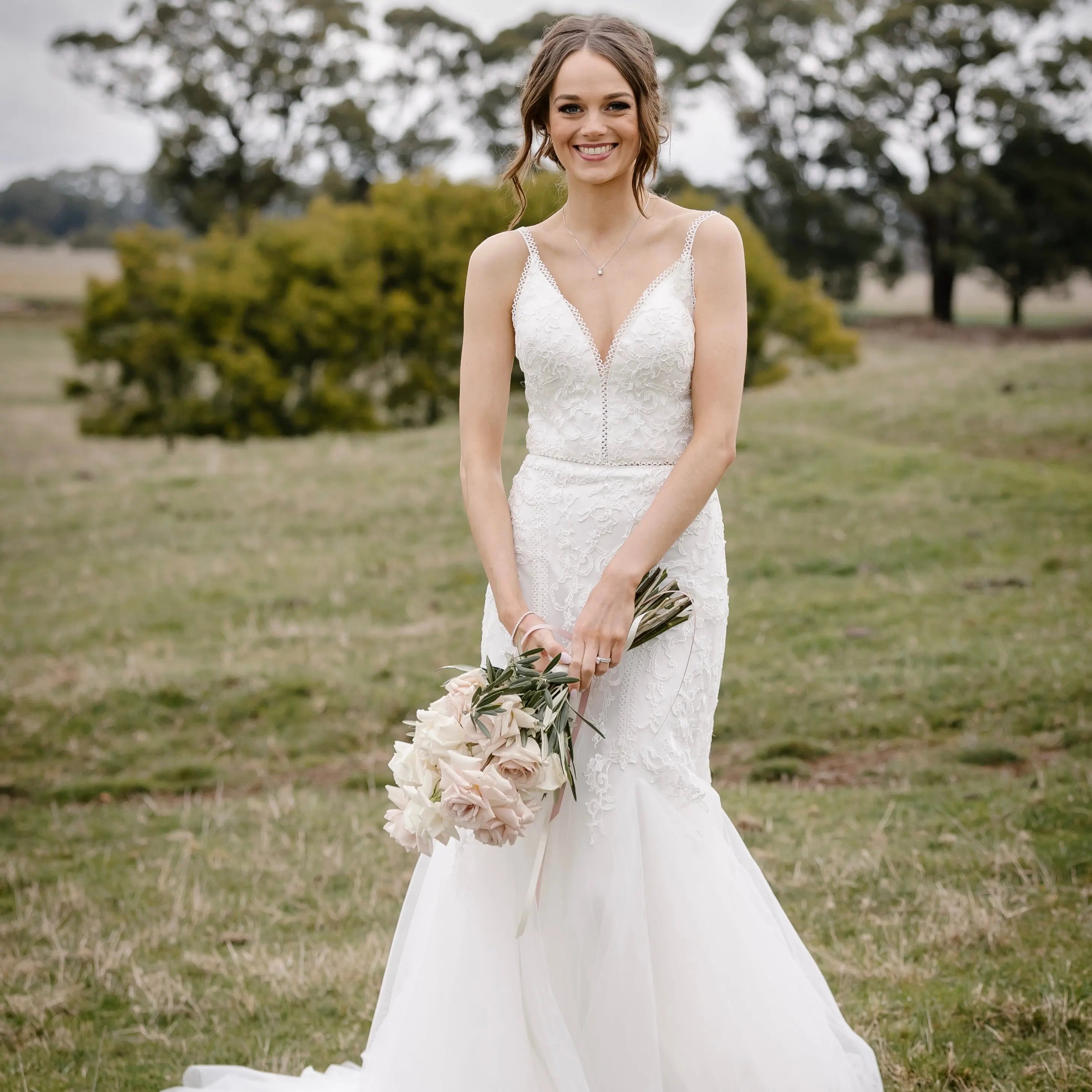 "A captivating and elegant Selena wedding gown, featuring a Boho-inspired design. The dress showcases a flattering V-neckline with delicate lace trim, intricate lace detailing throughout, and a fit and flare silhouette that accentuates the wearer's curves. The gown is completed with a chapel train and lace trim on the waist, creating a stunning bridal look."