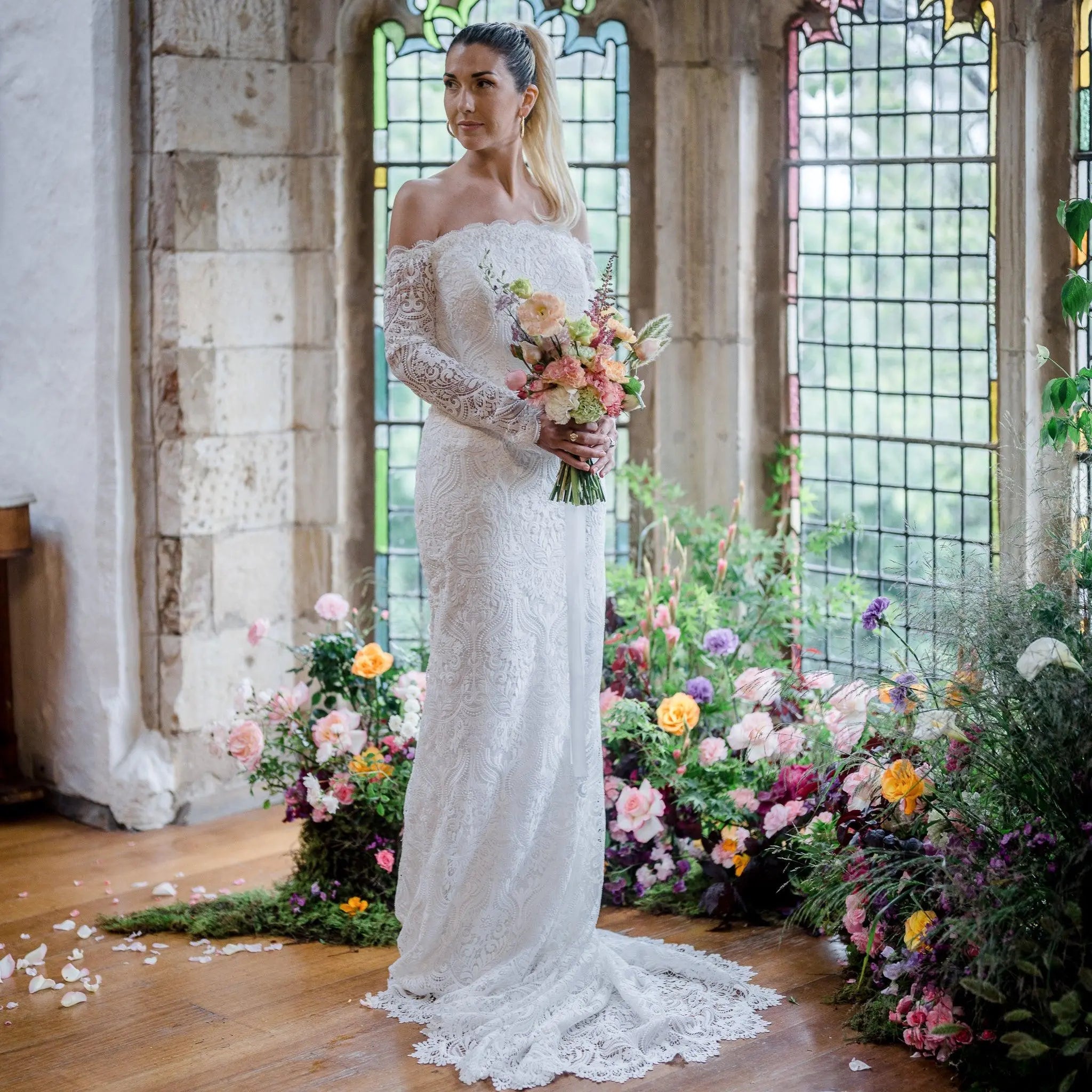 Stunning bride in the Celaya wedding dress featuring off-the-shoulder sleeves, scalloped trim, and a gracefully trailing chapel train.