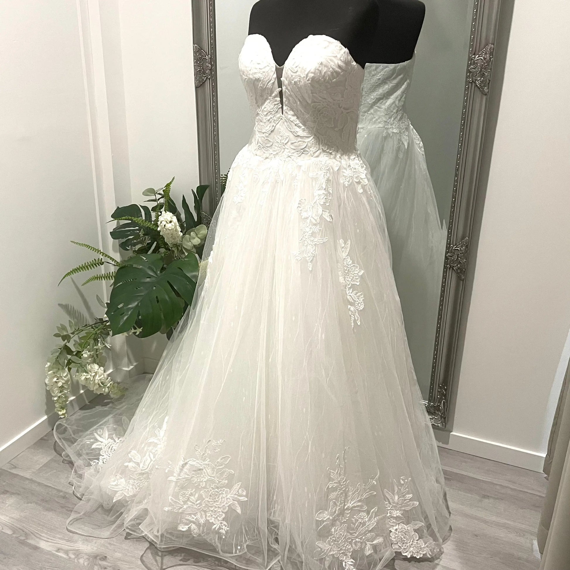 Detailed front view of the Kate wedding gown showcasing its strapless bodice with lace appliqué, flowing seamlessly into a classic ballgown skirt with intricate sequins and a patterned underlayer.